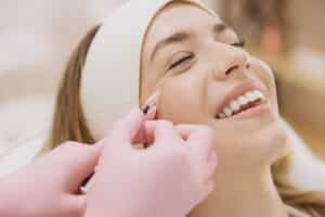Professional beautician administering Botox injection to smiling woman, targeting facial wrinkles during a cosmetic anti-aging treatment